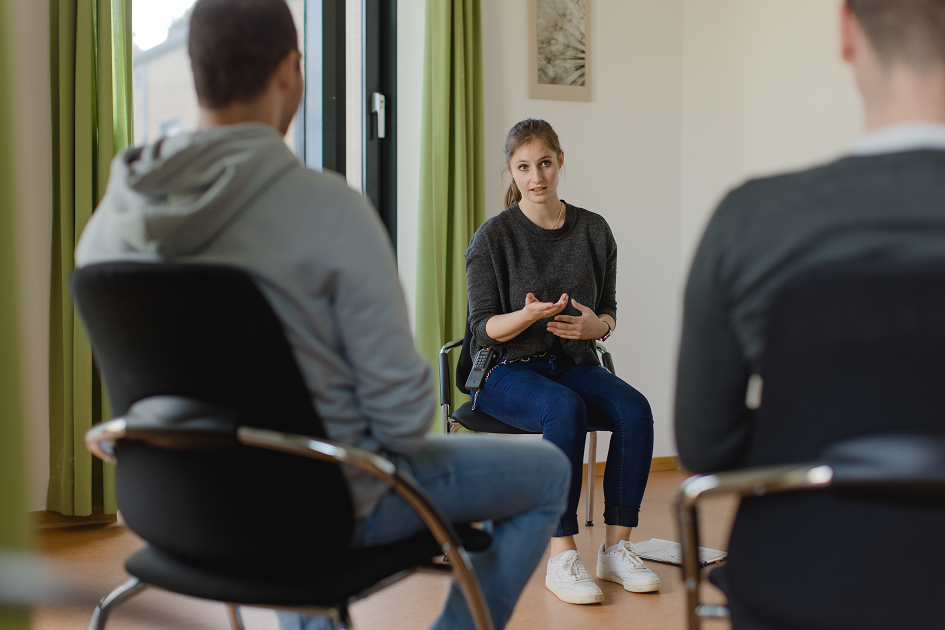 Eine Therapeutin in einer Sitzungssituation mit zwei Patienten.