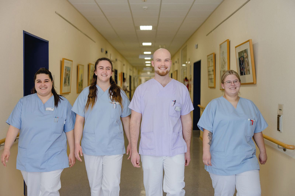Vier Pflegekräfte auf einem Stationsflur laufen auf die Kamera zu 