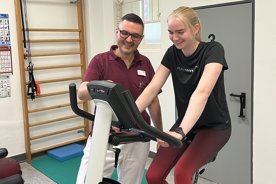 Eine Patientin sitzt auf einem Ergometer und wird von einem Arzt betreut.