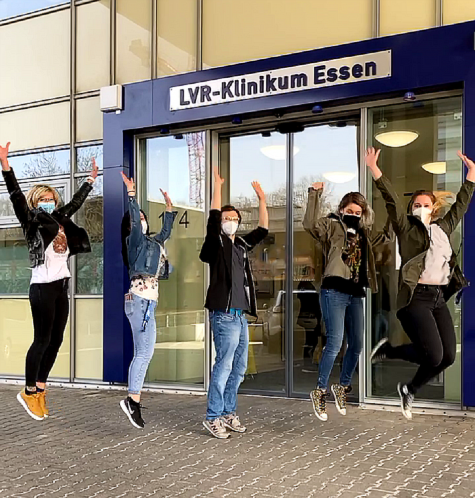 Fünf Mitarbeitende des LVR-Klinikums Essen springen vor dem Haupteingang in die Luft